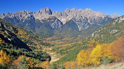 Autumnal mountain valley with vibrant foliage and majestic peaks under a clear blue sky