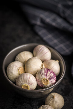 Solo glove garlic bulbs in bowl on black table.