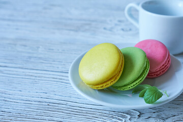 Colorful macaroons on a plate and cup of coffee on a wooden background