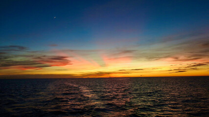 Colorful sunset over the sea. The sun's rays illuminate the sky from beyond the horizon. View of the calm surface of the sea and the sun's rays beyond the horizon.