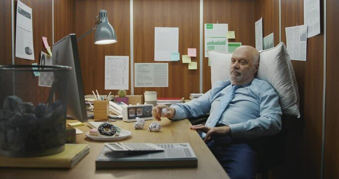 Bored inefficient employee sitting at his desk in a small office and wasting time