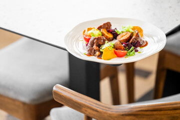 A beautifully plated dish featuring tender meat with colorful vegetables and greens, elegantly served on a stylish plate, perfect for a sophisticated dining experience.
