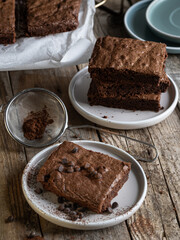 A slice of chocolate brownie garnished with cocoa and sprinkles. A stack of brownies in the background.