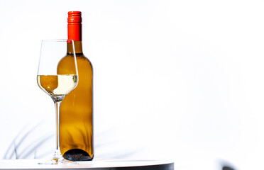 Non-alcoholic, alcohol free, white wine sauvignon blanc in glass with bottle. White background, palm leaves shadows, hard light