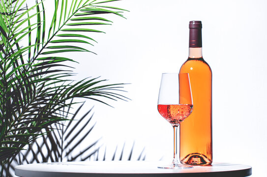 Non-alcoholic, alcohol free, pink rose wine pinot noir in glass with bottle. White background, palm leaves shadows, hard light