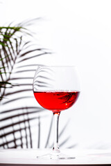 Non-alcoholic, alcohol fries,  pink rose wine grenache in glass with bottle. White background, palm leaves shadows, hard light