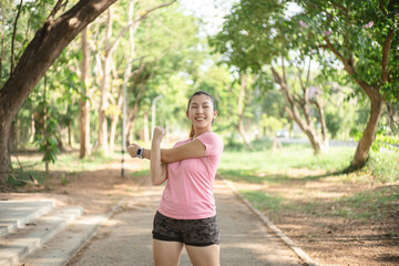An Asian woman warms up her muscles before going jogging in a park full of trees..