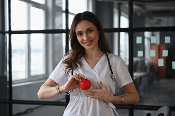 Cardiologist is holding toy heart. Woman doctor is in the office