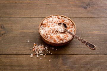 Coarse pink salt in wooden bowl and spoon and spilled salt. Cooking or spa concept