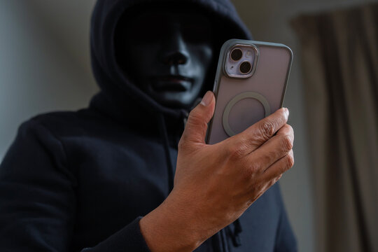 An anonymous masked hacker is using a smartphone to penetrate credit card financial information.