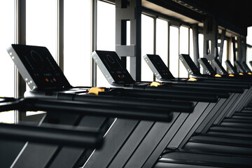 Horizontal photo of rows of treadmill machines in gym on the side of wide windows.