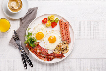 A classic breakfast plate featuring sunny-side-up eggs, crispy bacon, sausages, and fresh tomatoes