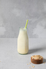 Refreshing oat milk smoothie with straw in glass bottle on gray surface. Detox