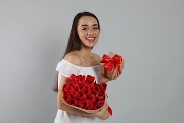 Happy woman with red tulip bouquet and gift box on light grey background. 8th of March celebration