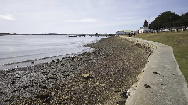 Gentle waves lapping rocky shoreline with serene cityscape of puerto williams nestled along beagle channel's pristine navarino island coastline