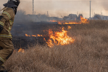 Adult man in a firefighter's uniform putting out a fire in an open field on a sunny day. Sharpness...