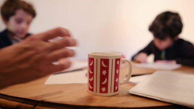 Mother helping two children with schoolwork while sitting at kitchen table, creating nurturing home learning atmosphere