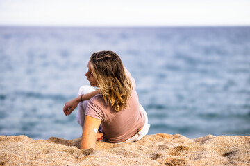 Woman wearing continuous glucose monitor relaxing on beach enjoying ocean view