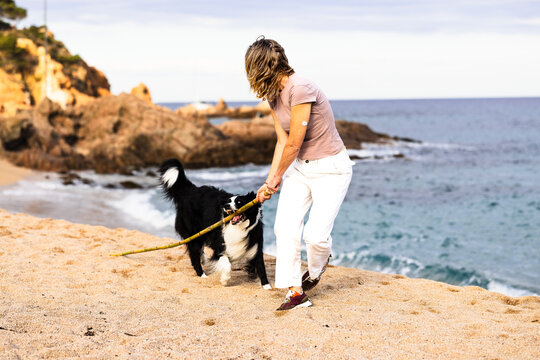 Mature woman with CGM playing with her border collie dog on a sandy beach at Costa Brava. Spain