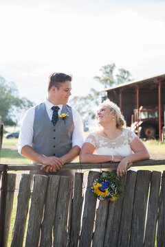 Groom and Bride looking at each other leaning on farm fence