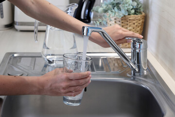 Teenage girl filling a glass with fresh tap water from a kitchen faucet for drinking. 