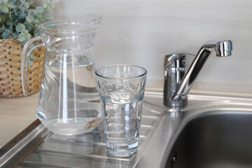 Tap water pitcher and glass on a kitchen counter near a sink with plant.