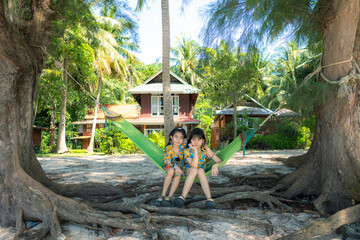 A young couple relaxing on a hammock in a green park surrounded by trees, smiling and enjoying nature with a child nearby The scene is peaceful, with people barefoot, having fun in the summer outdoors