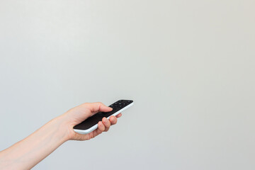 A young woman in a white T-shirt using a remote control to turn on the TV or air conditioner. Empty space for text
