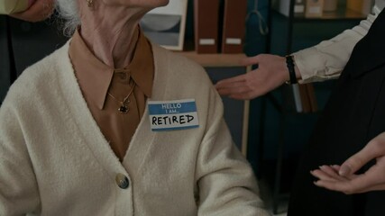 Closeup of unrecognizable office colleague gently pinning Retired badge onto senior woman sweater, marking her transition and celebrating her career