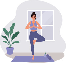 Fototapeta premium Woman practicing yoga indoors in tree pose on purple mat near plant and window 