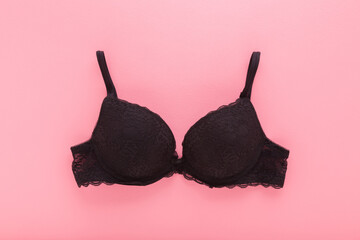New dark black lace bra on light pink table background. Pastel color. Female casual underwear....