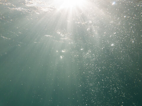 Sunrays underwater with sparkling bubbles in blue pool water 