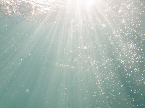 Sunrays underwater with sparkling bubbles in blue pool water 