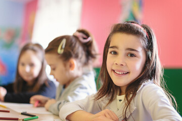 Cute girls in the classroom drawing and smiling for camera