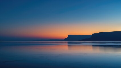 Fototapeta premium The peaceful desert landscape under a twilight sky with shades of blue and orange reflected on a salt flat, silhouette of mountains adding tranquility.