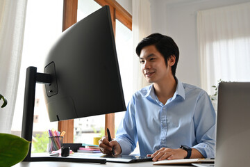 Young man using a digital pen and tablet while working on a large monitor in a bright office setting