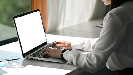 Close-up of a professional woman working on a laptop in a bright, modern workspace. Hands on keyboard, focusing on remote work