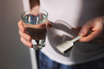 Man hands with a scoop with collagen or protein powder and a glass of water. Trendy beauty supplement for healthy skin and bones.