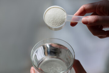Woman hands with a scoop with collagen or protein powder and a glass of water. Trendy beauty supplement for healthy skin and bones.