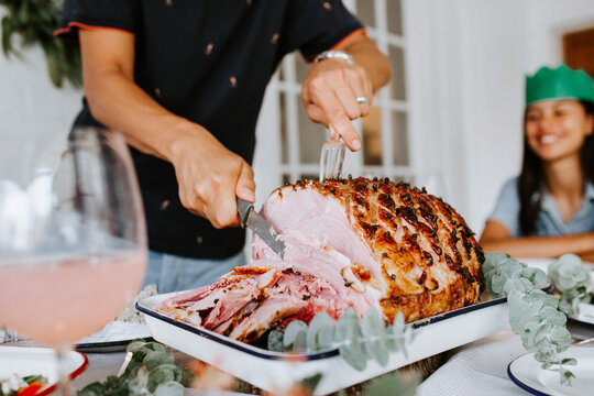 Middle aged man making thin cuts of roasted ham on the table