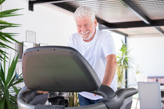 Happy and active senior white haired man doing exercises in the gym area running on the tapis roulant - healthy lifestyle for retired people