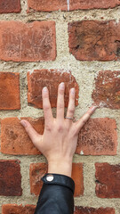 Woman's hand, featuring a silver ring and black jacket cuff, rests against weathered red brick...
