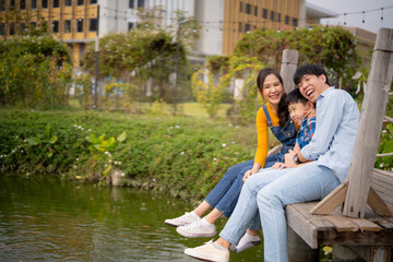Naklejka premium Young Asian happy family enjoy admired view at city park. Woman man and boy looking at scene, share laugh and smile in green summer garden. AI edited.