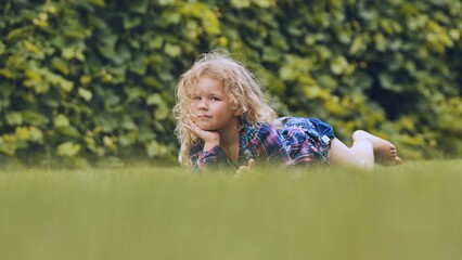 Obraz premium Blond girl reclining on verdant grass, basking in family moments amid natural park landscape, radiating carefree summer happiness