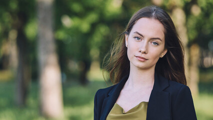 Confident businesswoman standing in park, professional attire reflecting success amid lush green landscape