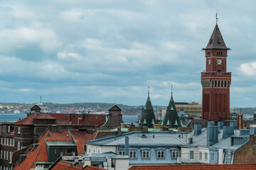 Obraz premium Elevated perspective shows Helsingborg's skyline. Rådhuset clock tower above diverse rooftops. City overlooks the Öresund strait towards Denmark under cloudy Swedish sky, creating an atmospheric scene
