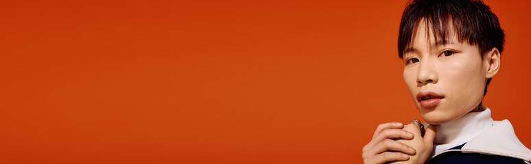 A stylish young man stands against a bright orange backdrop, radiating charm and confidence.