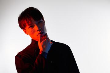 An elegant young Asian man poses captivatingly in a studio, exuding intrigue and confidence.