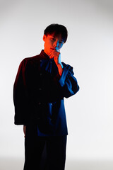 A young Asian man stands thoughtfully, displaying his stylish outfit and vibrant colors.