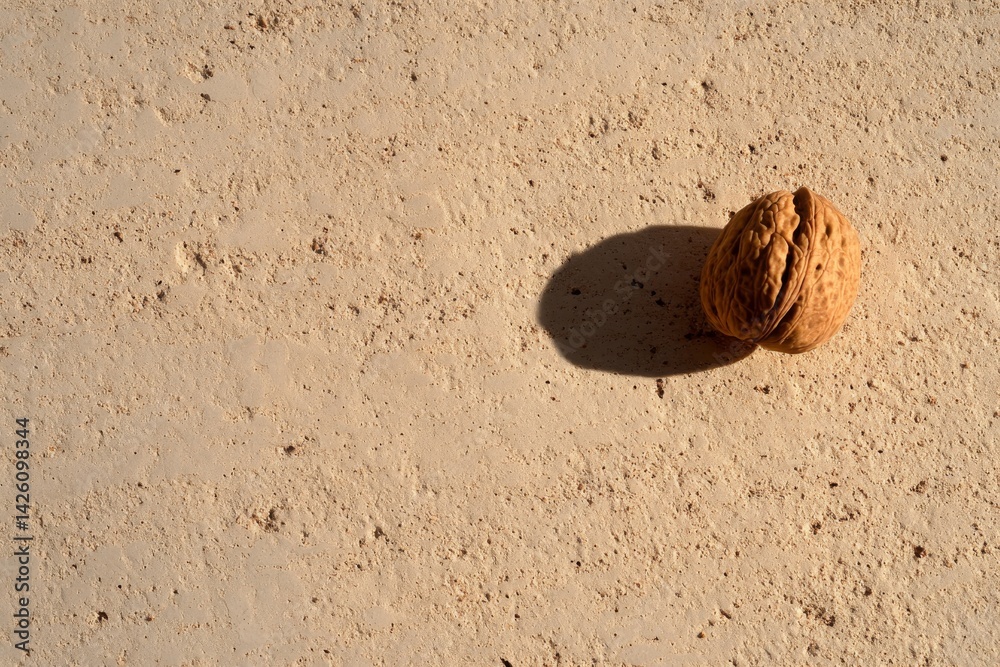 Aufkleber A cracked walnut rests on a soft beige surface, surrounded by scattered crumbs and subtle shadows, showcasing natural textures and ample copy space for text